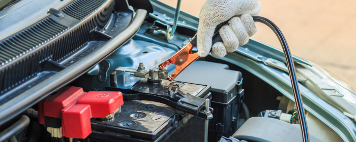 Gloved hand attaching a jump cable to a car battery
